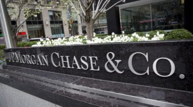 A large black stone sign with silver letters reads JPMorgan Chase & Co. in front of a city office building with white flowers and greenery in the background. | esgnews.com