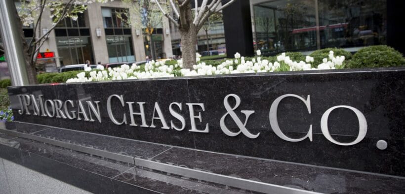 A large black stone sign with silver letters reads JPMorgan Chase & Co. in front of a city office building with white flowers and greenery in the background. | esgnews.com